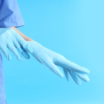 Woman doctor putting on gloves on blue background