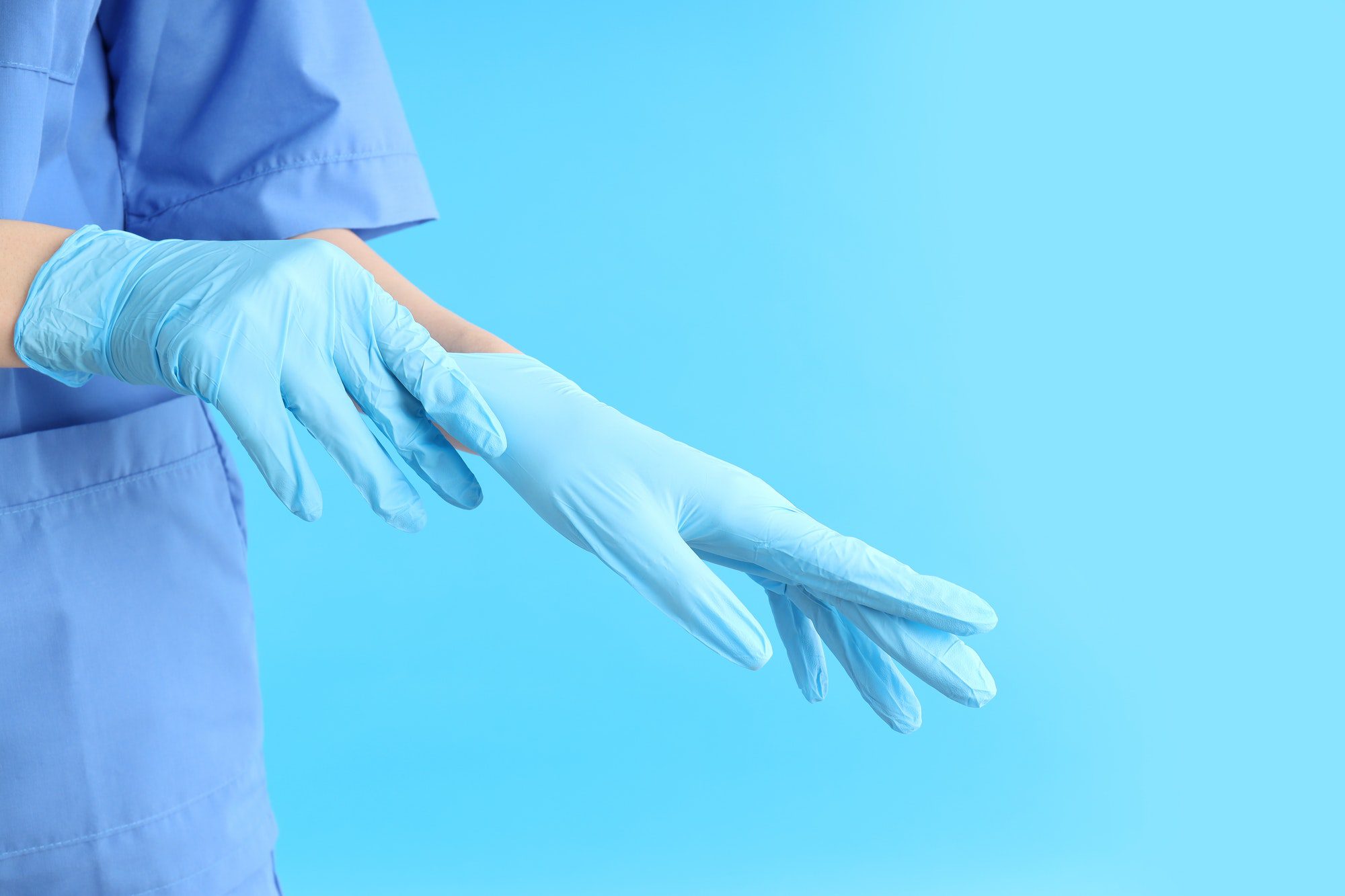 Woman doctor putting on gloves on blue background